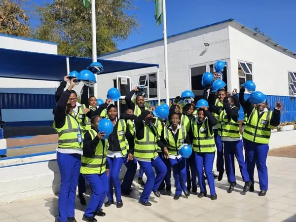 PMT students in safety vests and blue pants holding blue hard hats in front of a white building.